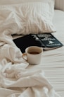 A cup of coffee and a book on a bed