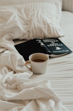 A cup of coffee and a book on a bed