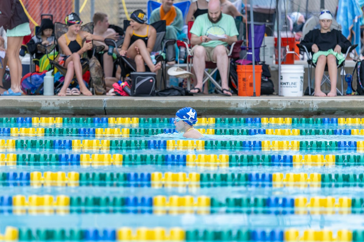 A group of swim team members sitting on a bench by a pool, discussing summer swim team organization strategies.