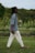 A man walking across a lush green field holding a glass of wine