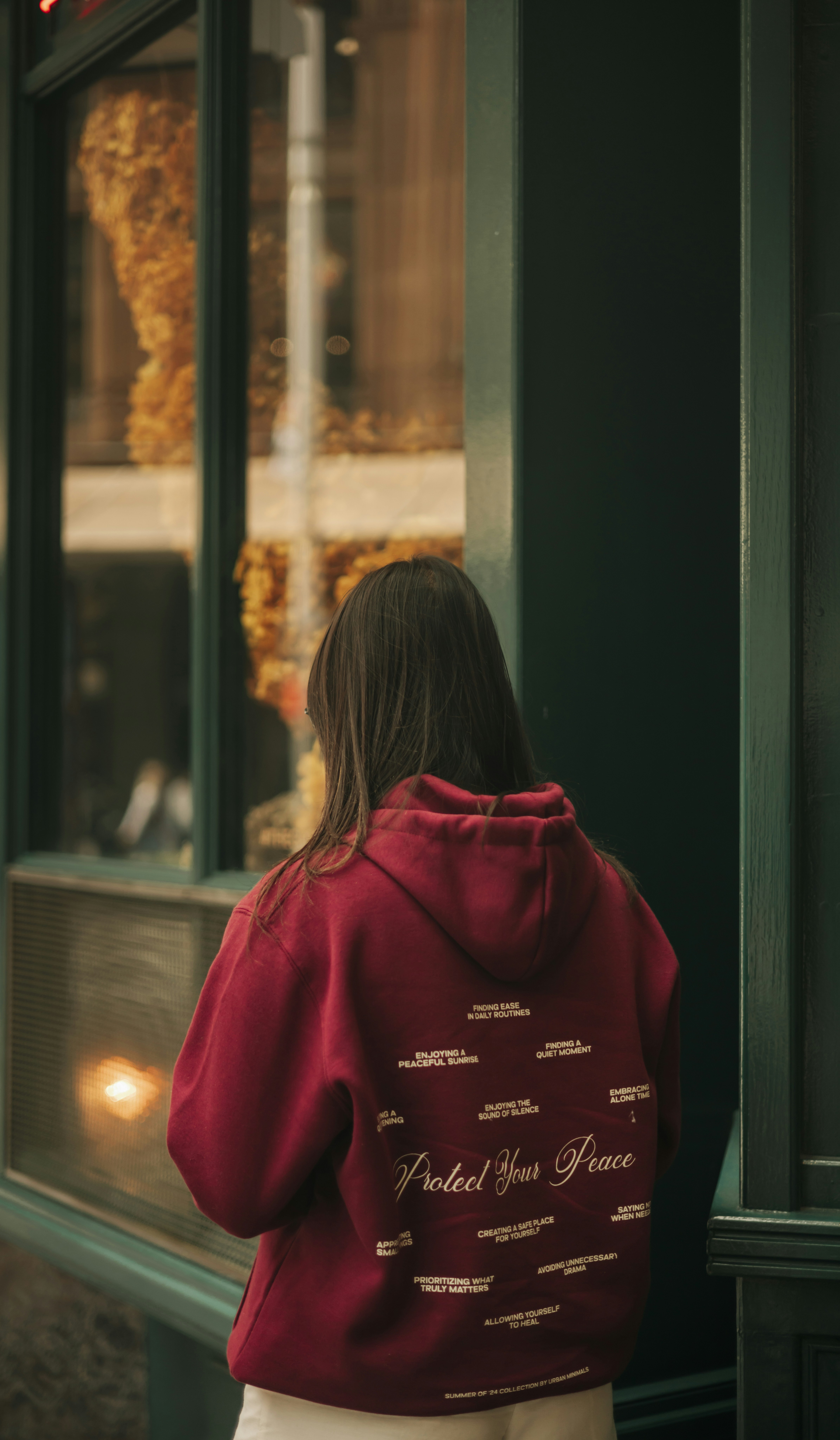A woman in a red hoodie looking out a window