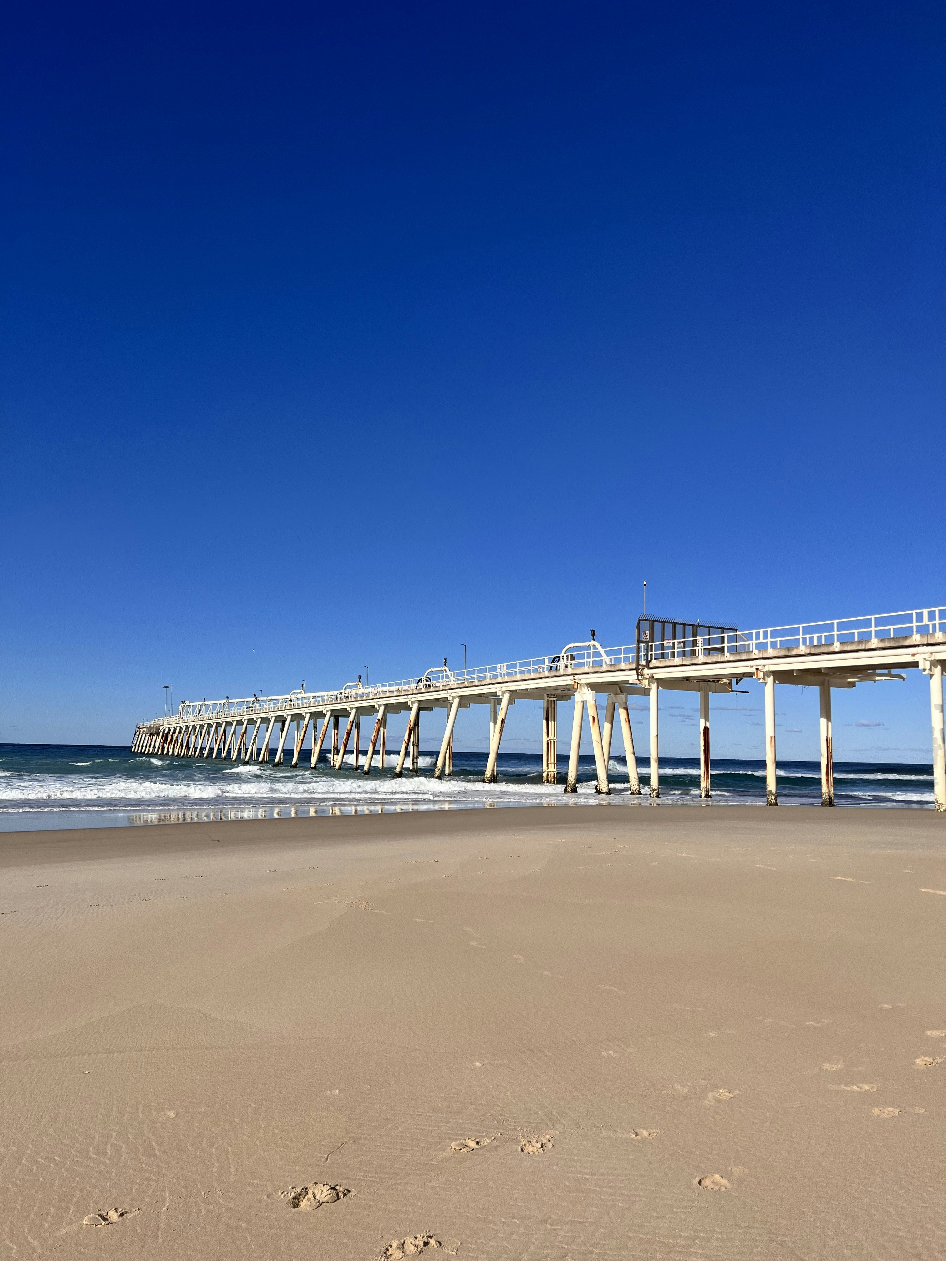 A pier on a beach with footprints in the sand