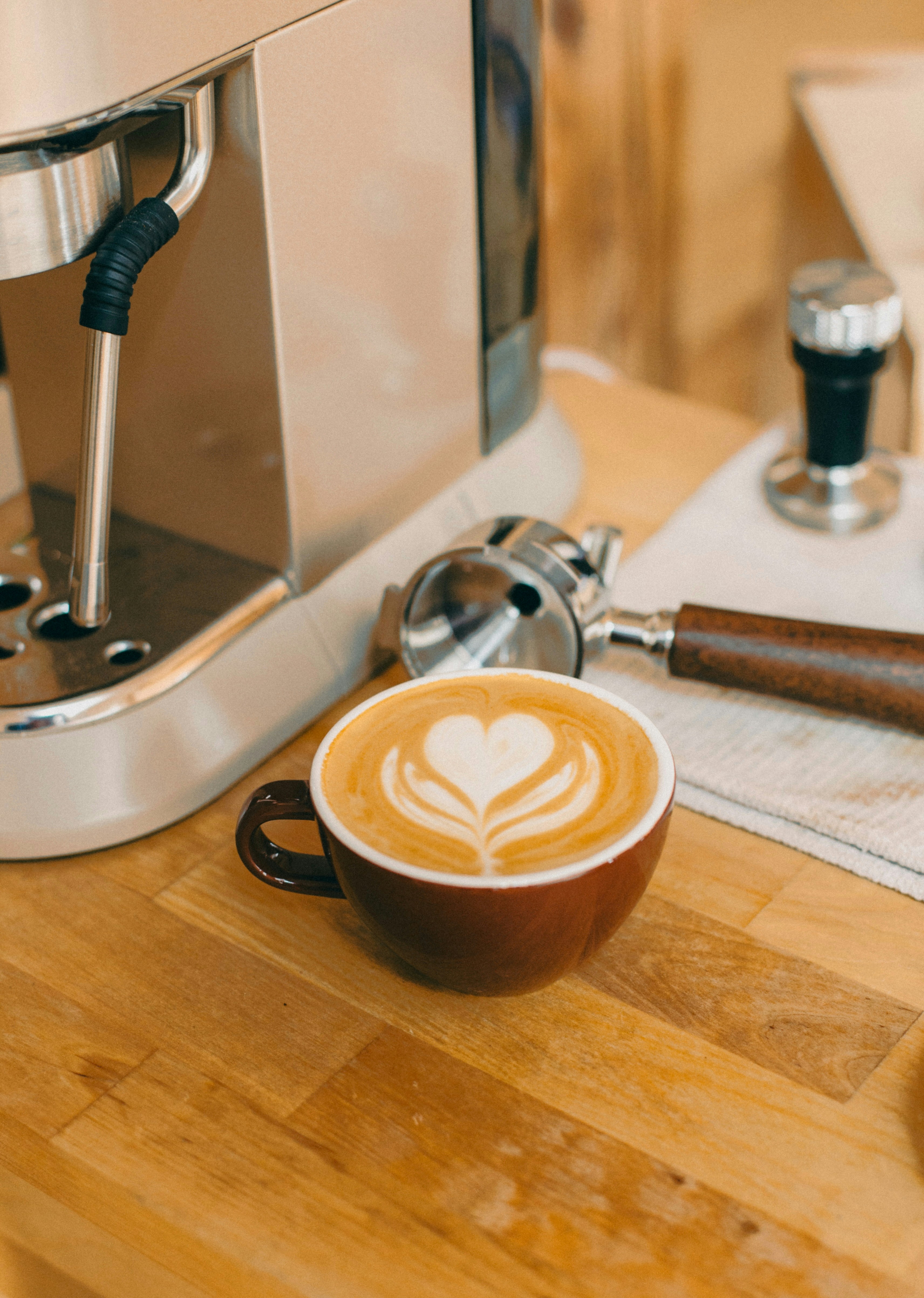 A cappuccino sits on a table next to a coffee maker
