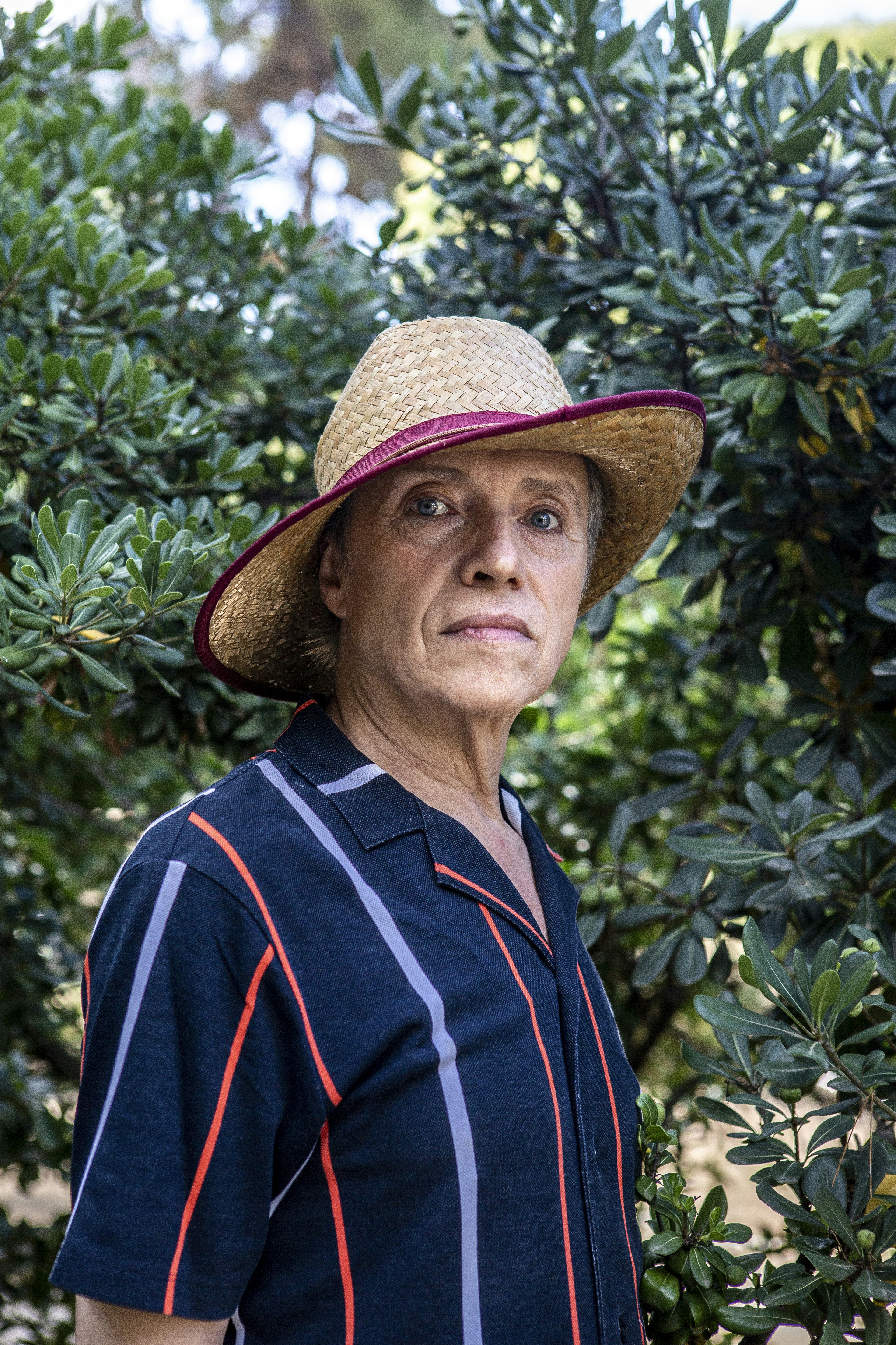 A woman wearing a hat standing in front of a bush