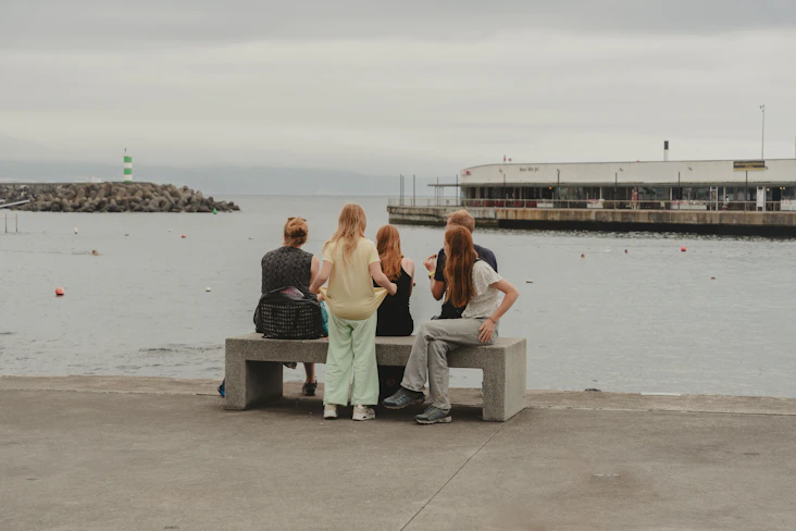 A group of people sitting on a bench next to a body of water