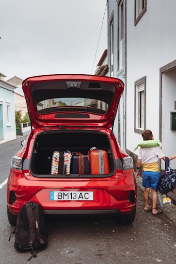 A red car with its trunk open on the side of the road