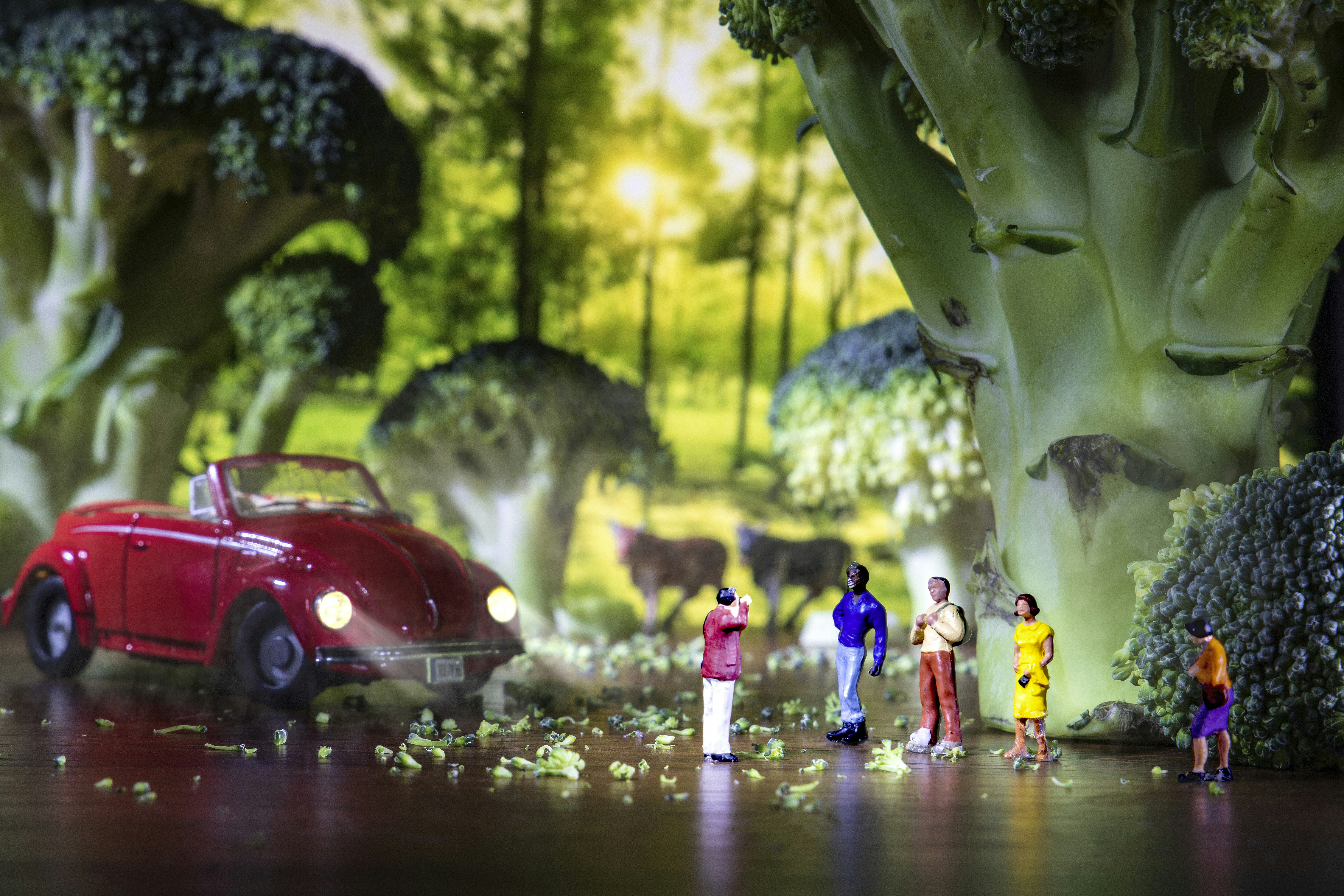 A group of miniature people standing next to a red car