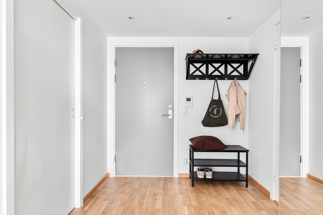 Organized apartment entryway with black wall-mounted coat rack with hooks and shelf, a shoe rack bench with shoes underneath, and tote bag hanging