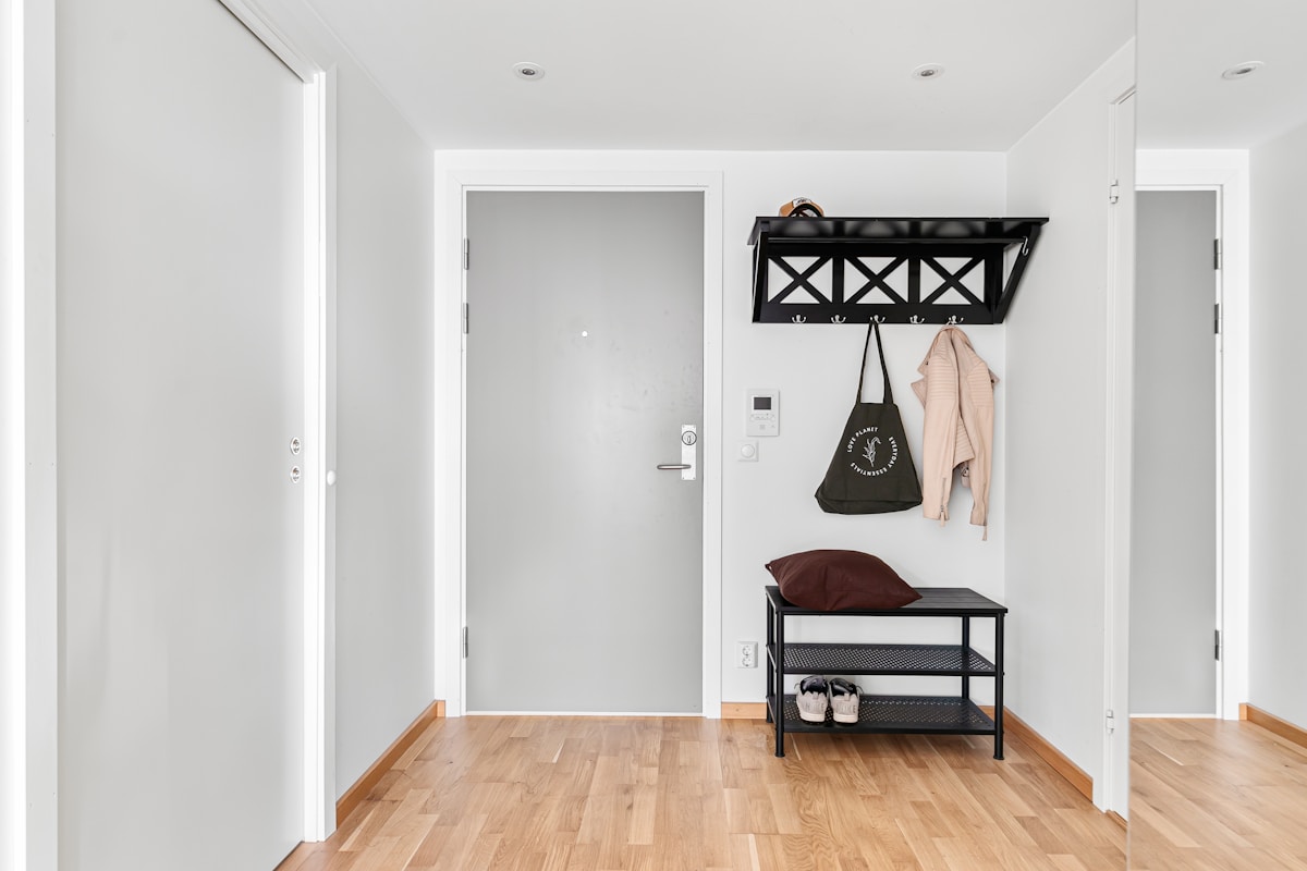 Clean modern apartment hallway entryway with wall-mounted black coat rack with hooks and a slim bench with lower shoe storage shelf