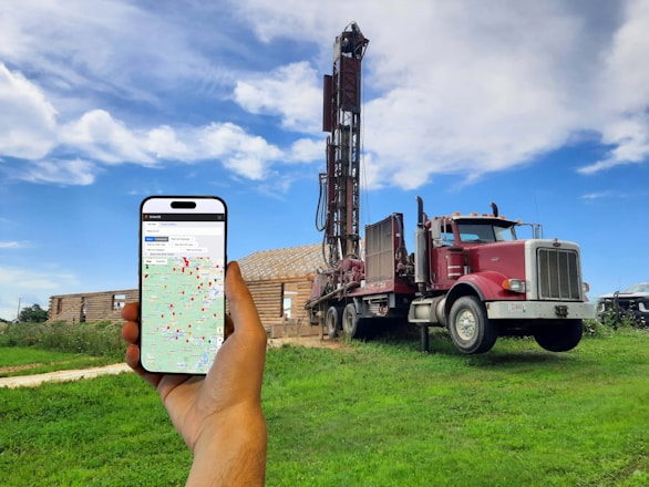 A person holding a cell phone in front of a drilling rig