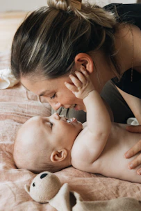 A woman is playing with a baby on a bed