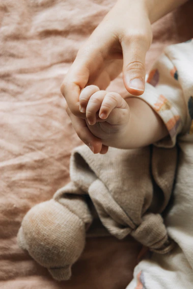 A person holding a baby's hand on top of a bed