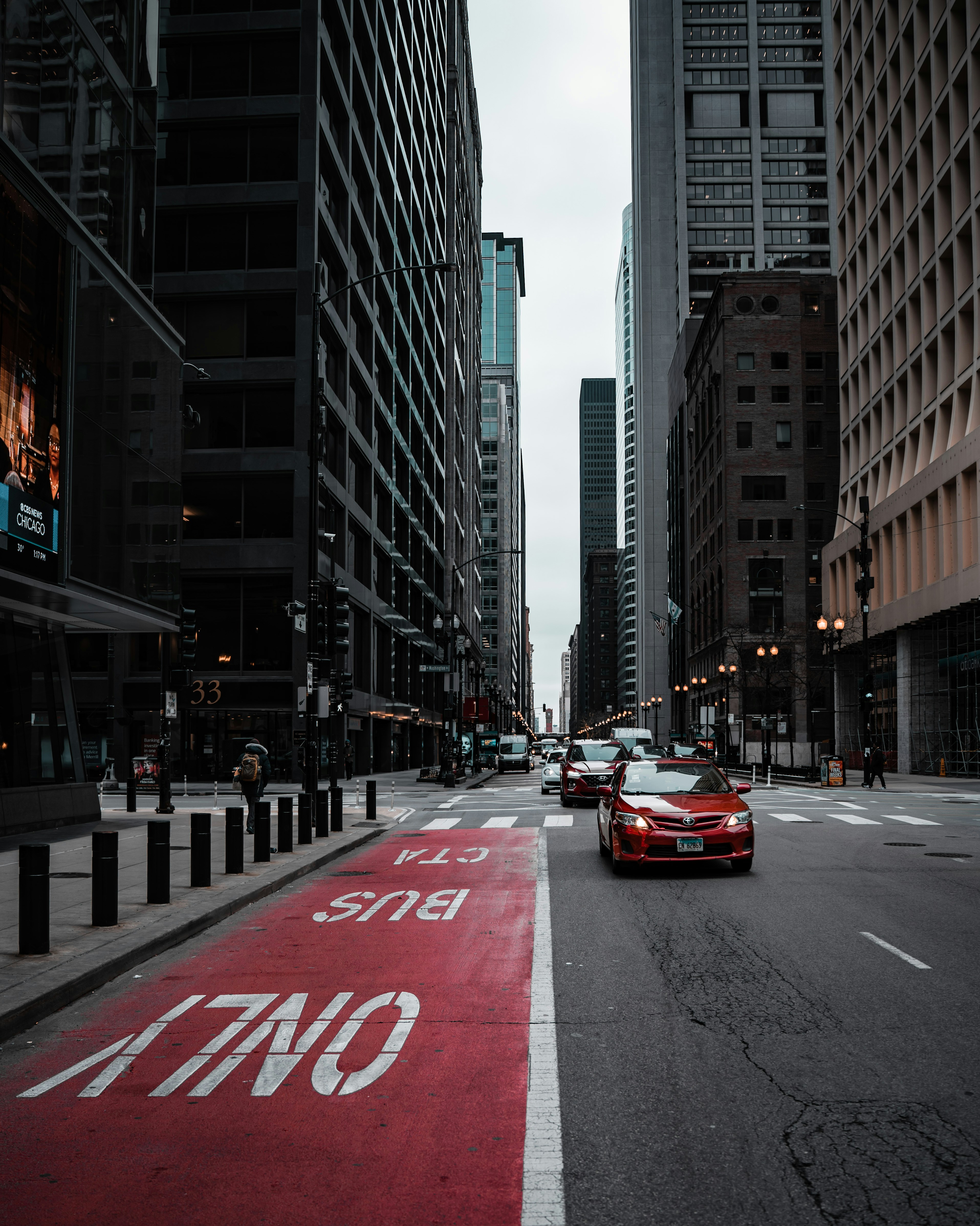 A red car driving down a street next to tall buildings