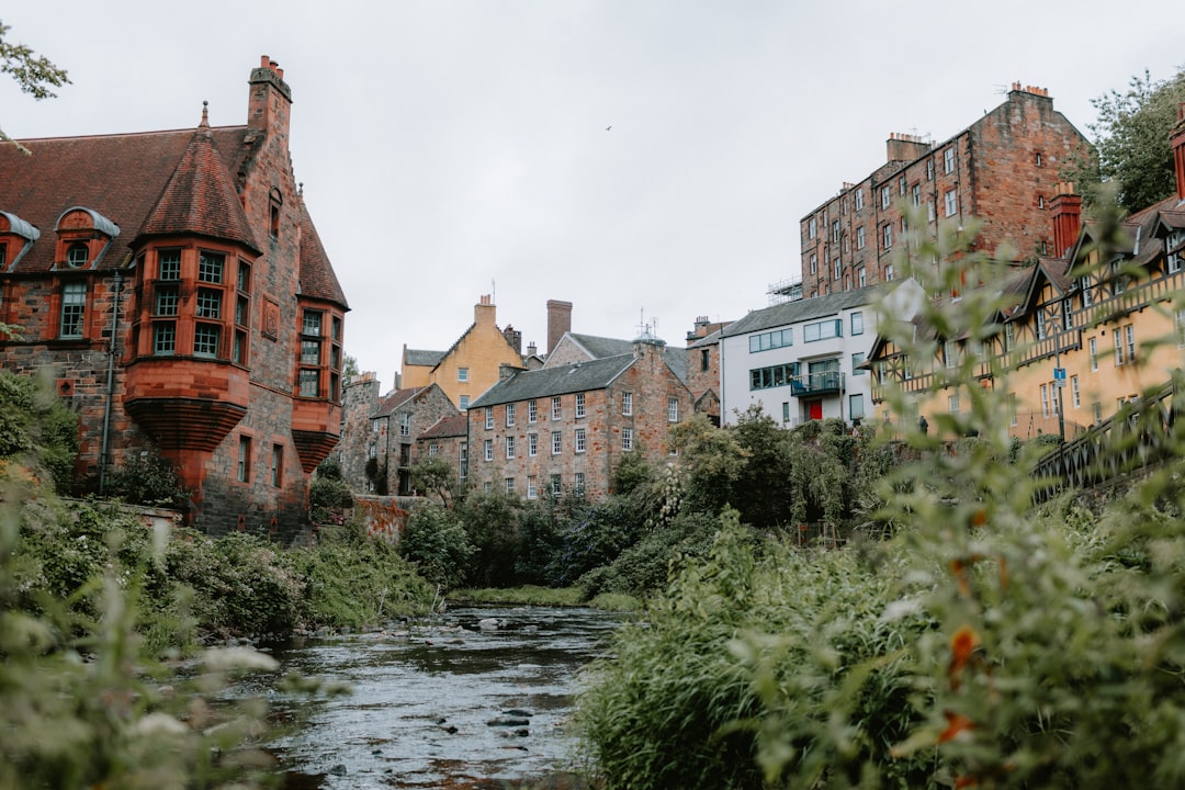 A river running through a lush green forest next to tall buildings,
