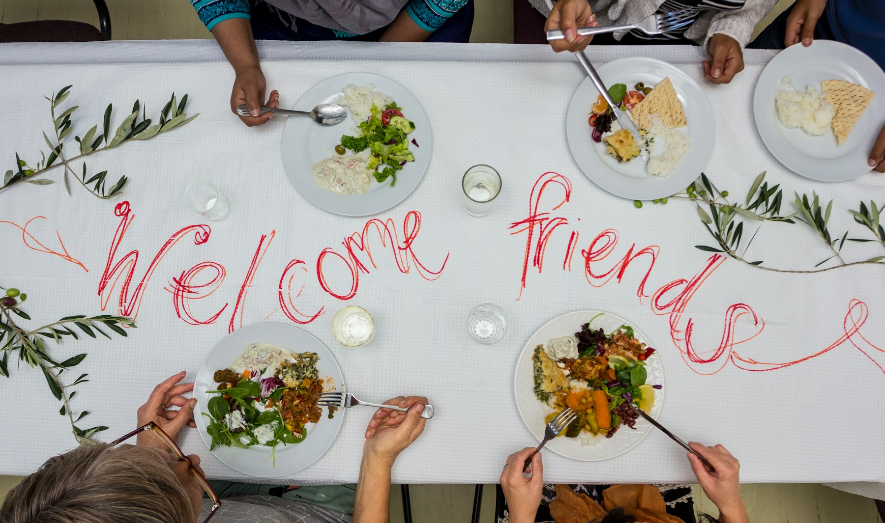 Overhead view of friends sharing a meal at a table with a handwritten Welcome friends message