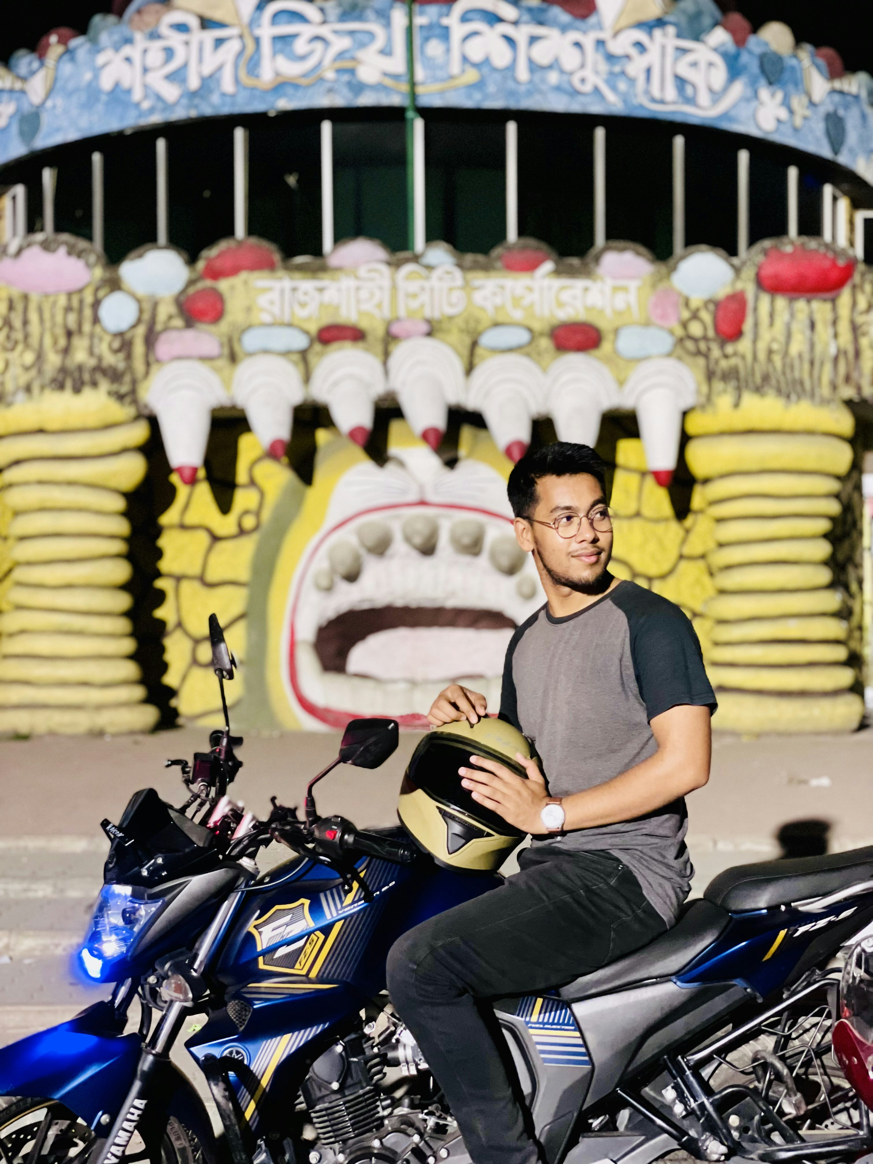 Seorang pria duduk di atas sepeda motor di depan wahana karnaval