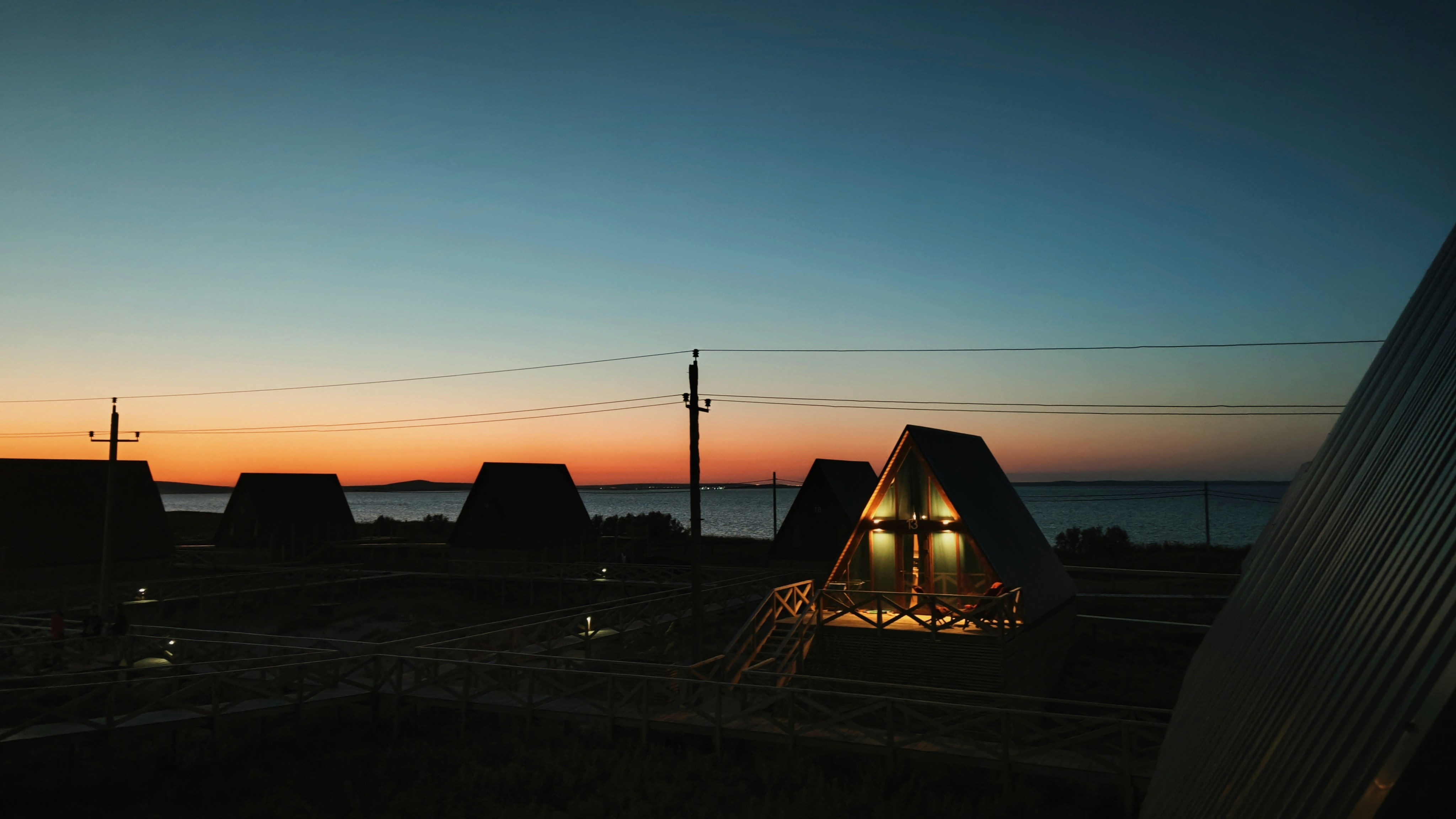 A group of A-frame cabins sit by a dark lake.