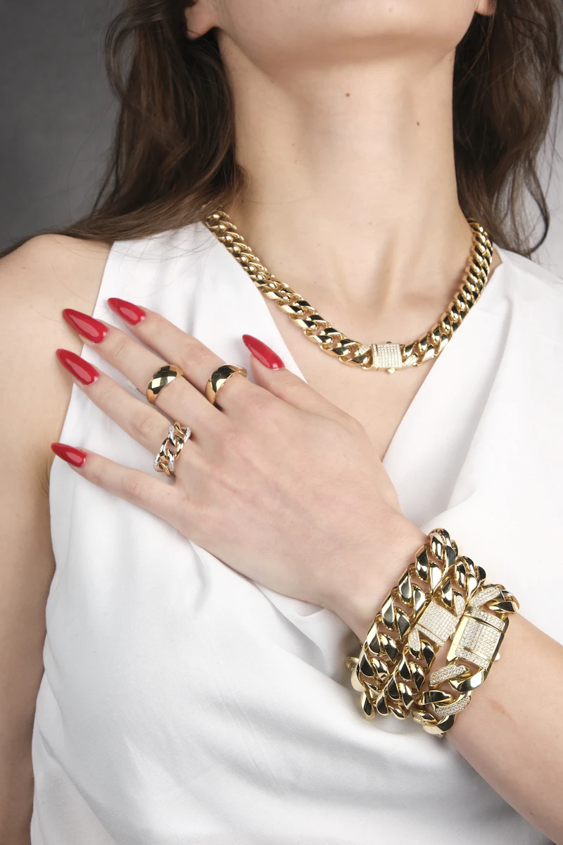 Adult woman's hands in a white shirt wearing a gold chain necklace, rings and chain bracelet