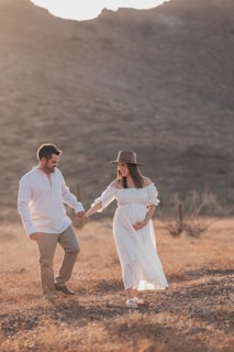 A pregnant couple holding hands in a field