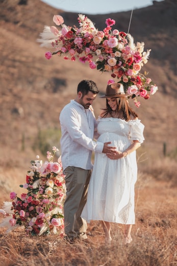 A pregnant couple standing under a floral arch