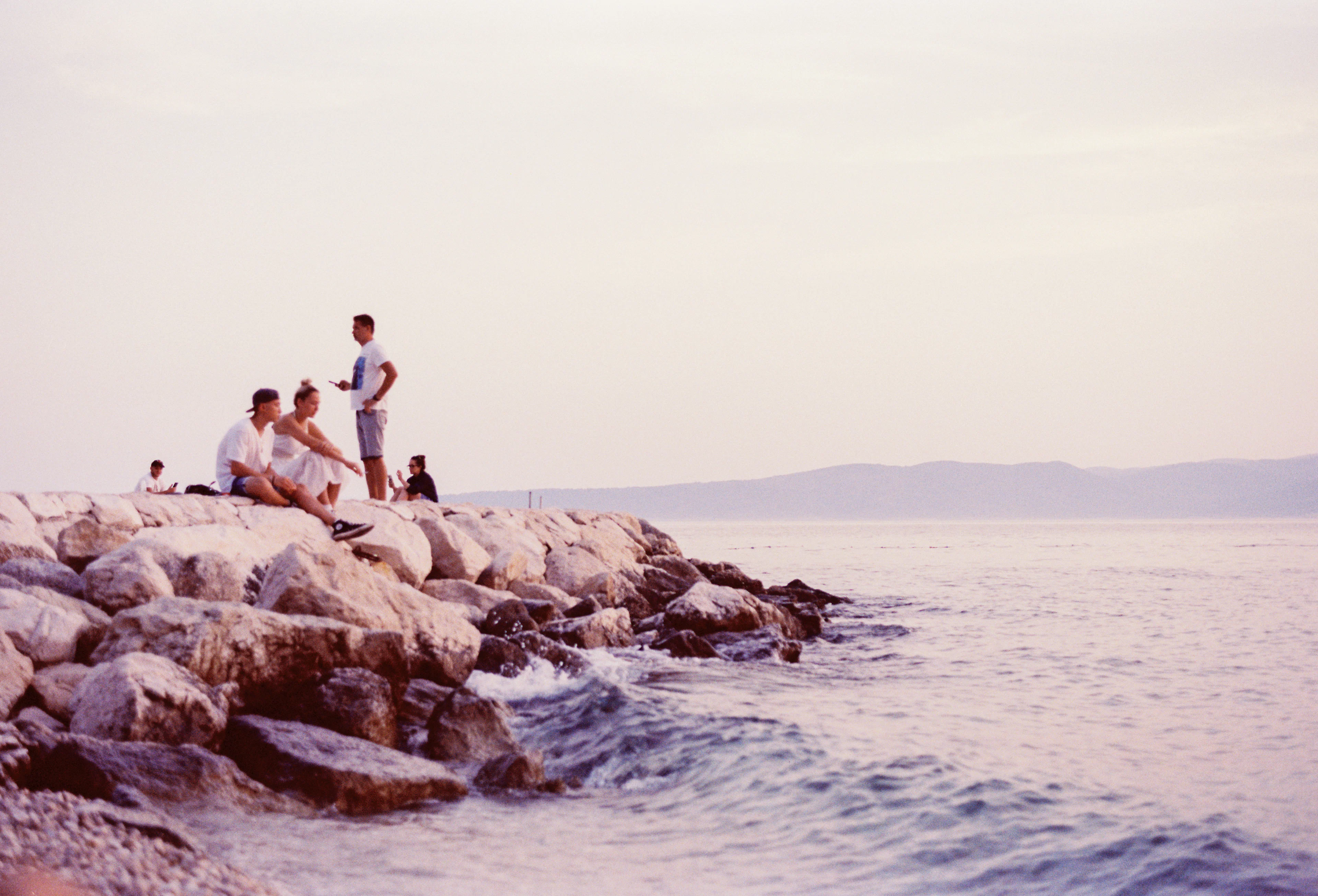 Une bande d'amis assis sur les rochers, au bord d'une mer pâle