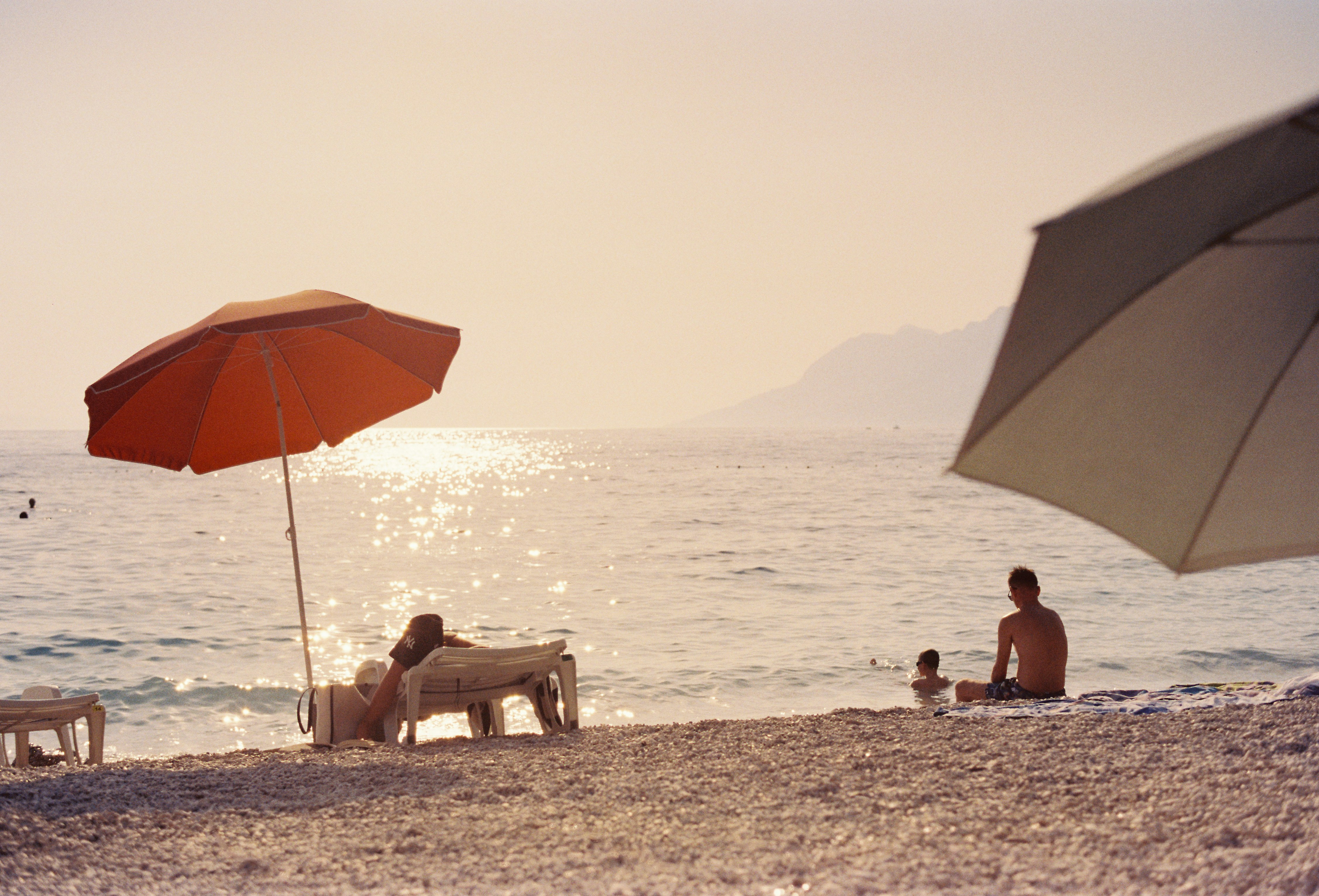 A group of people sitting on top of a sandy beach, Photo from Tungsten film roll taken with my AGFA Selectronic 3 on my trip to Croatia.