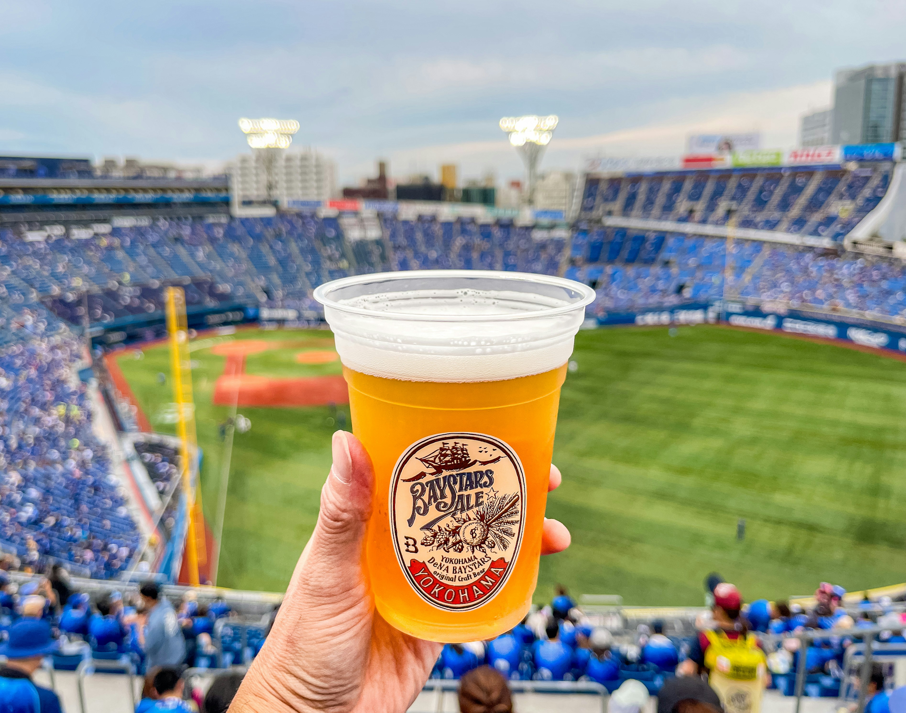 A person holding up a cup of beer at a baseball game