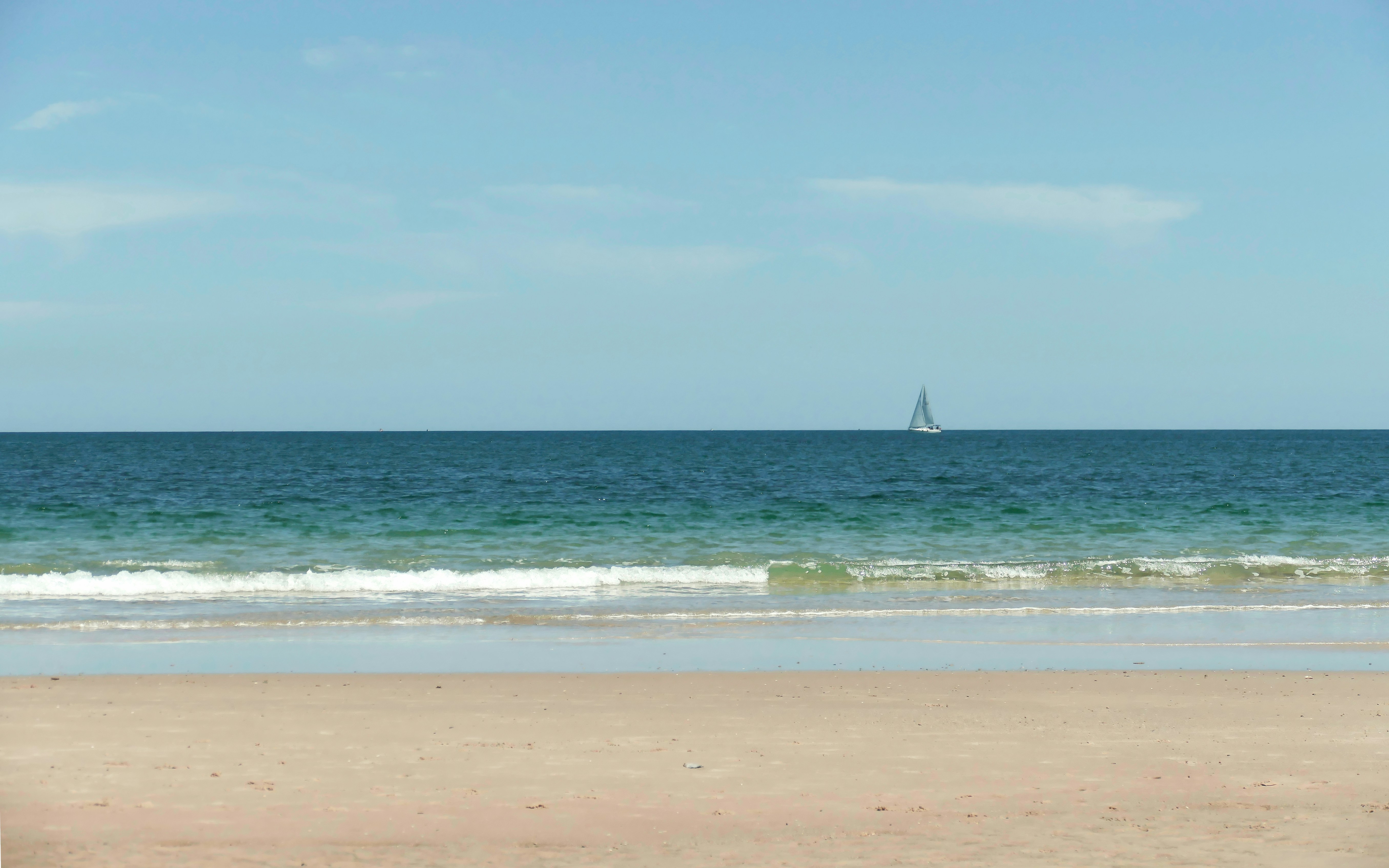 A view of a beach with a sailboat in the distance, Glenelg South Beach with Sailboat on Horizon