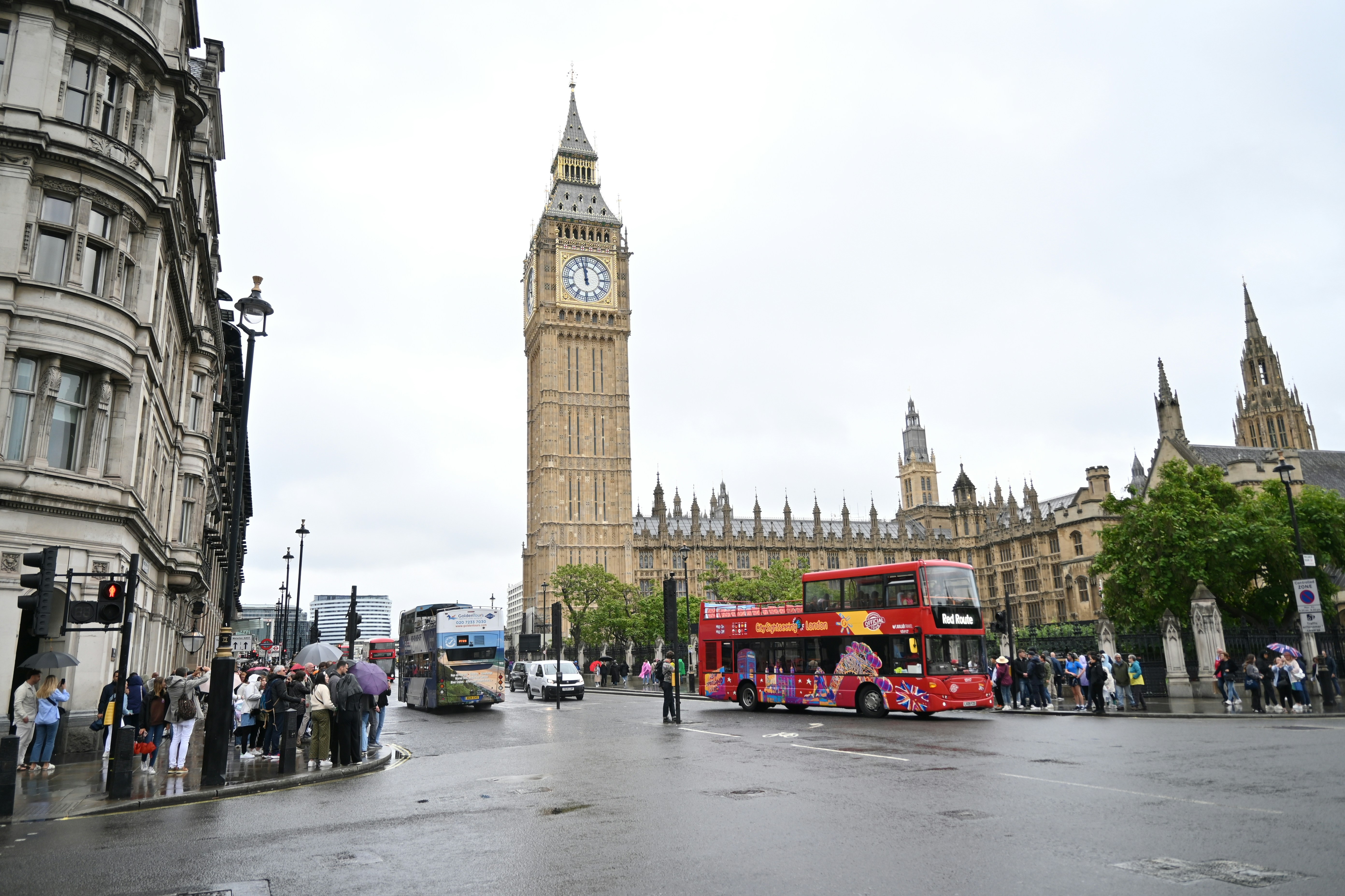 A red double decker bus driving down a street next to tall buildings