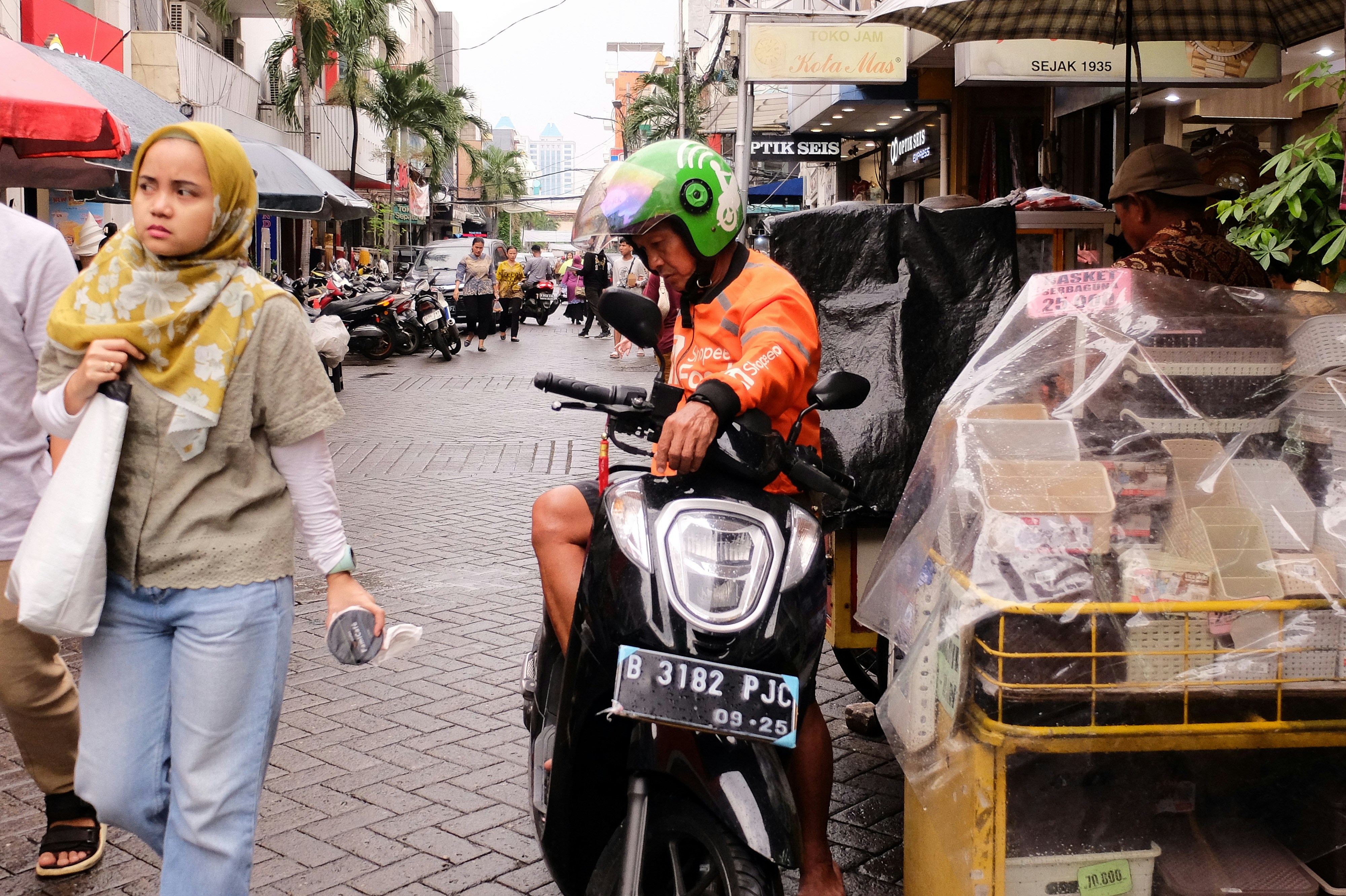 Seorang wanita berjalan di jalan di sebelah seorang pria dengan skuter