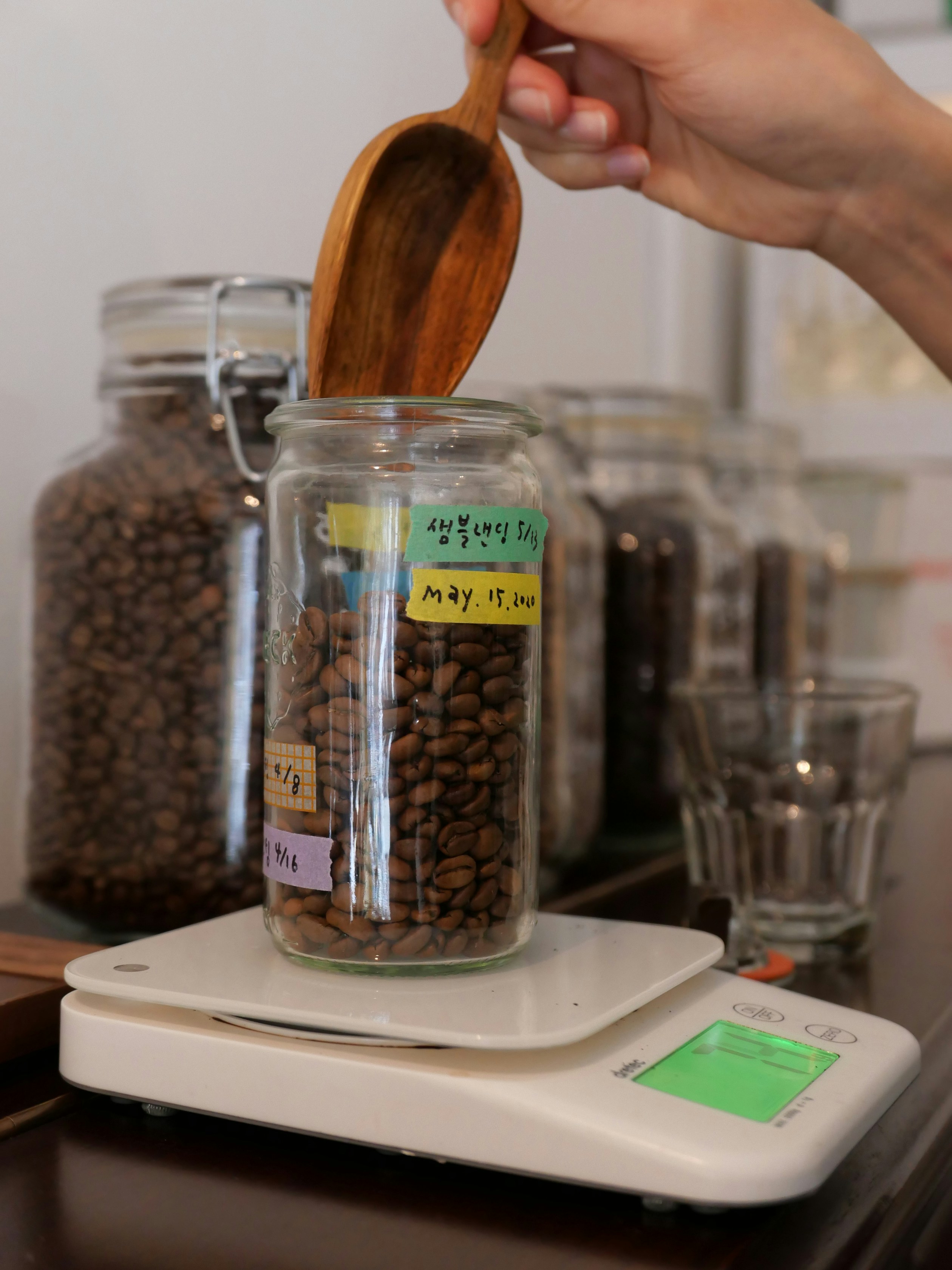 A person holding a wooden spoon over a jar of coffee beans