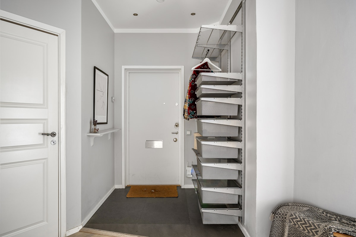 Scandinavian apartment entryway with white front door and space-saving pull-out storage system