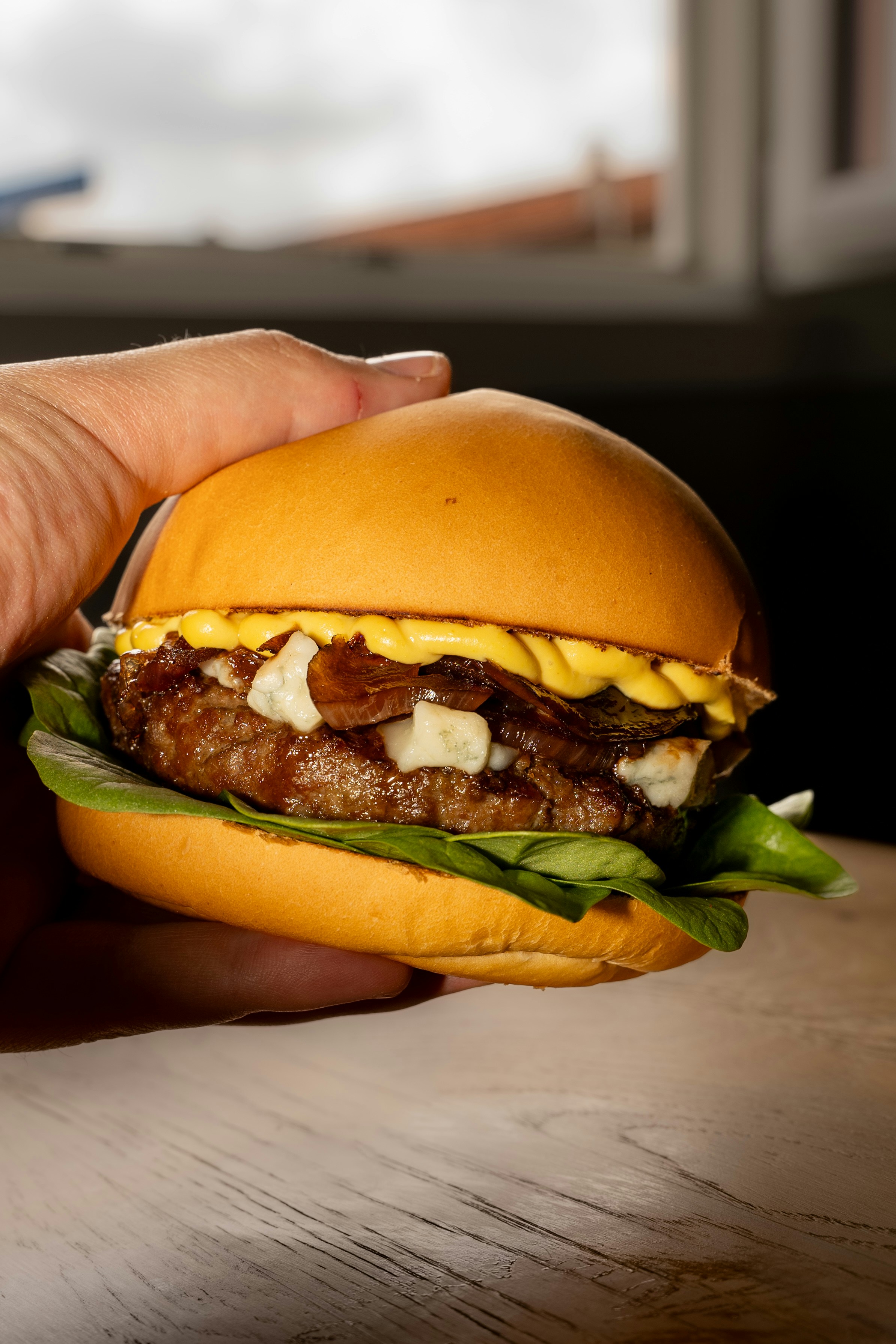A hand holding a hamburger on a wooden table