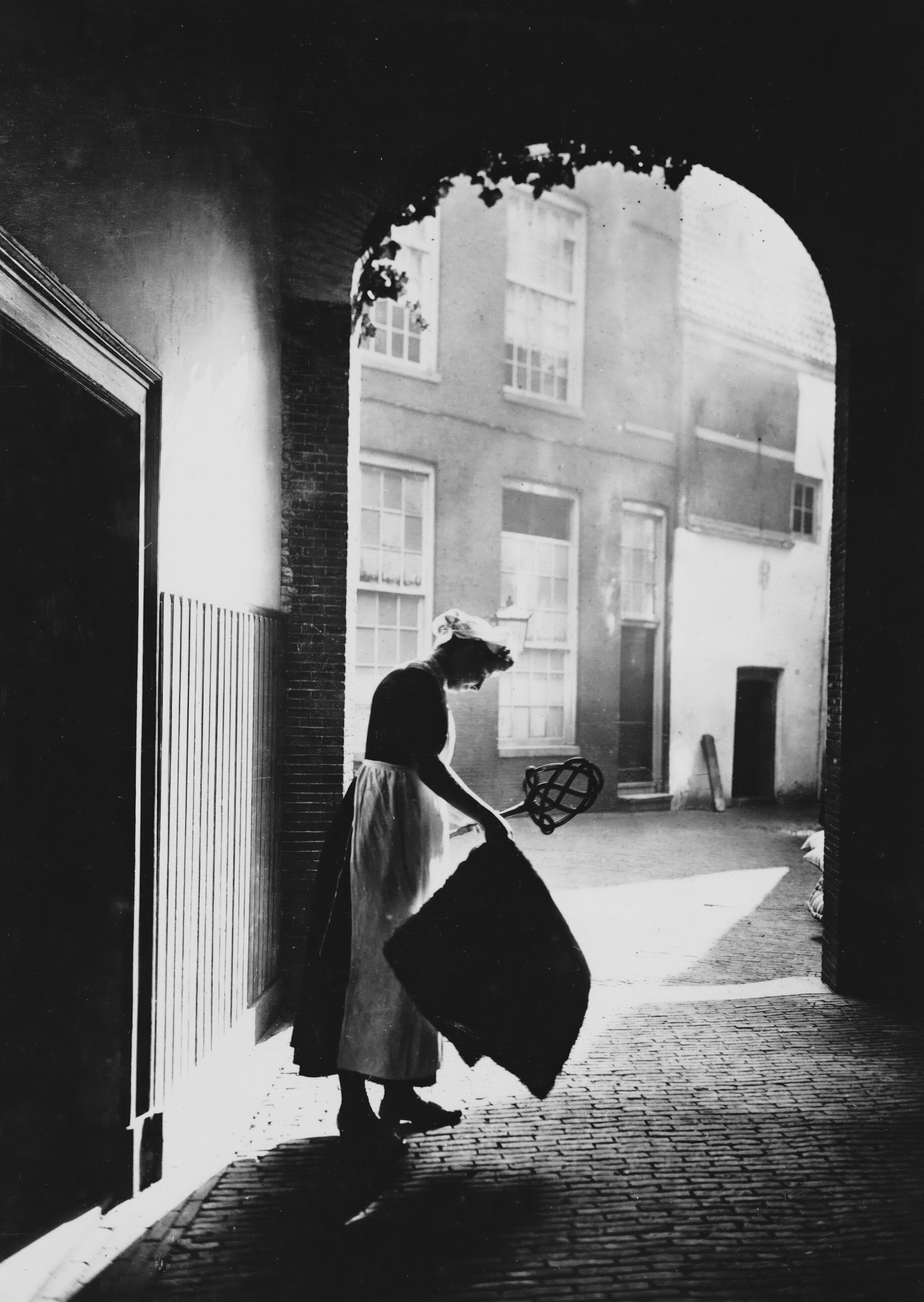 Woman in historical clothing sweeps courtyard.