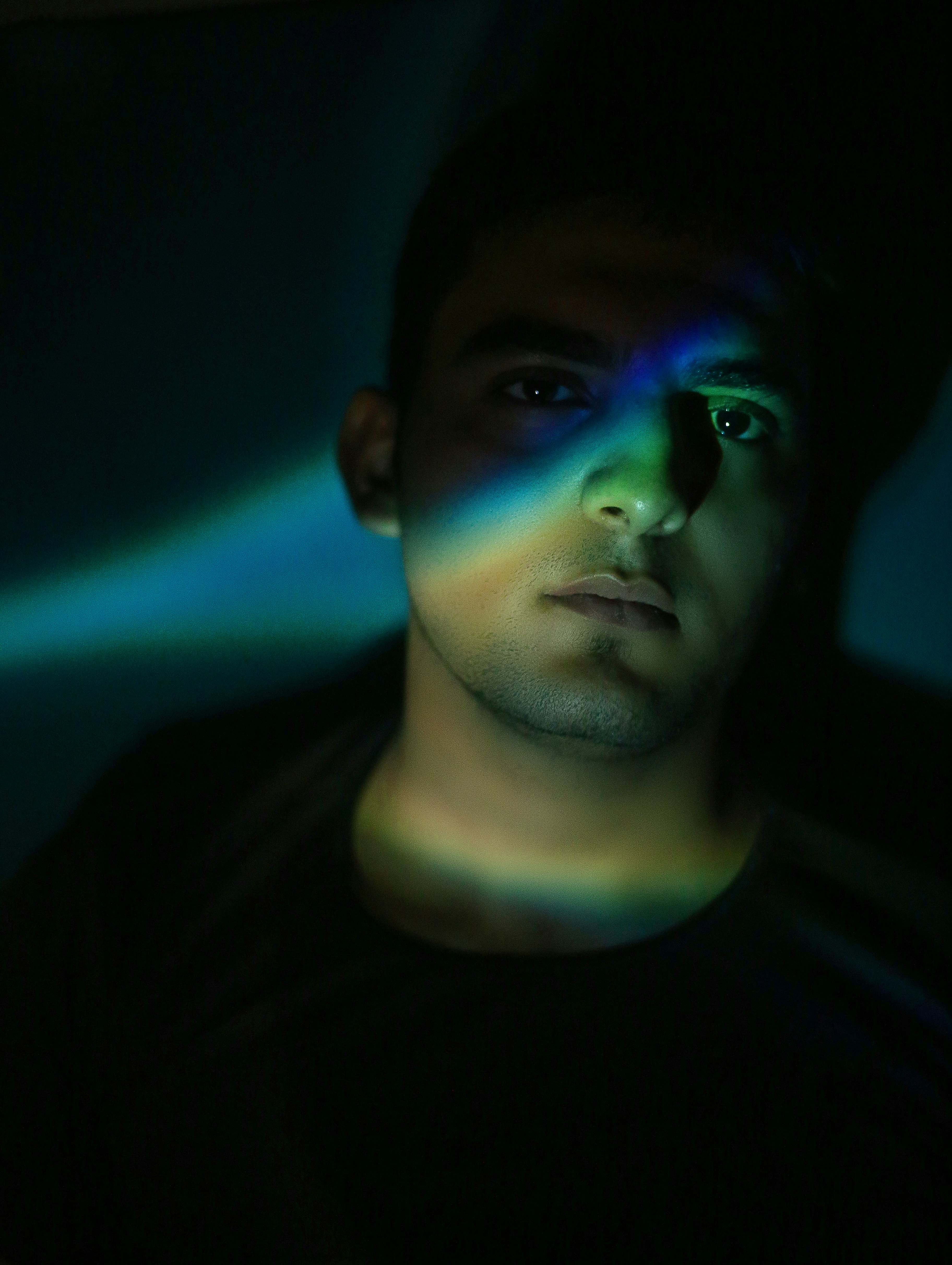 A man with a black shirt and a blue and green light on his face