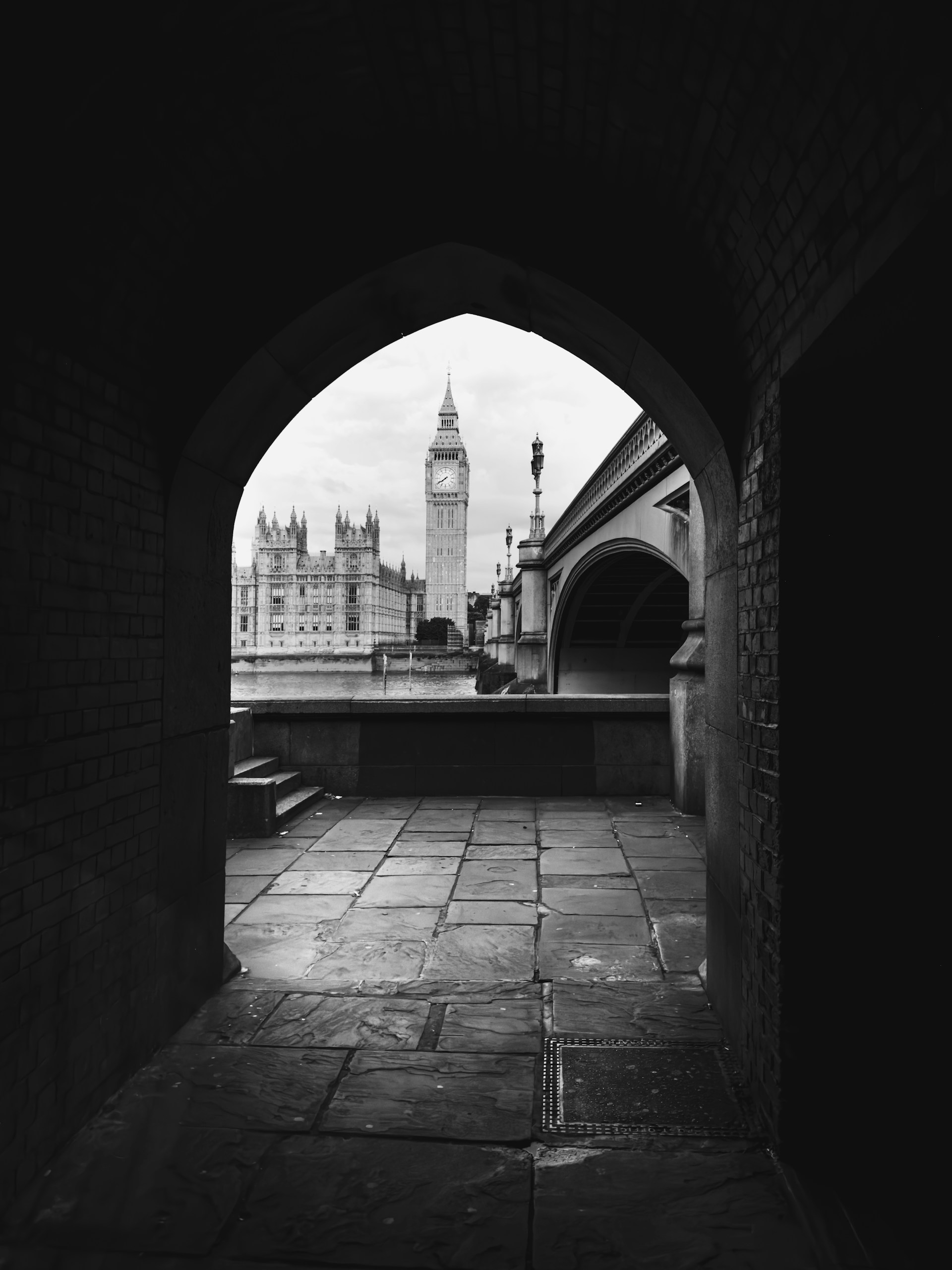 A black and white photo of a tunnel with a clock tower in the background