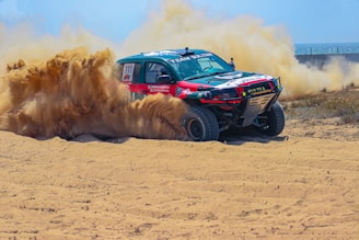 A truck driving through a sandy area with dust coming out of it