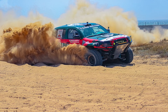 A truck driving through a sandy area with dust coming out of it