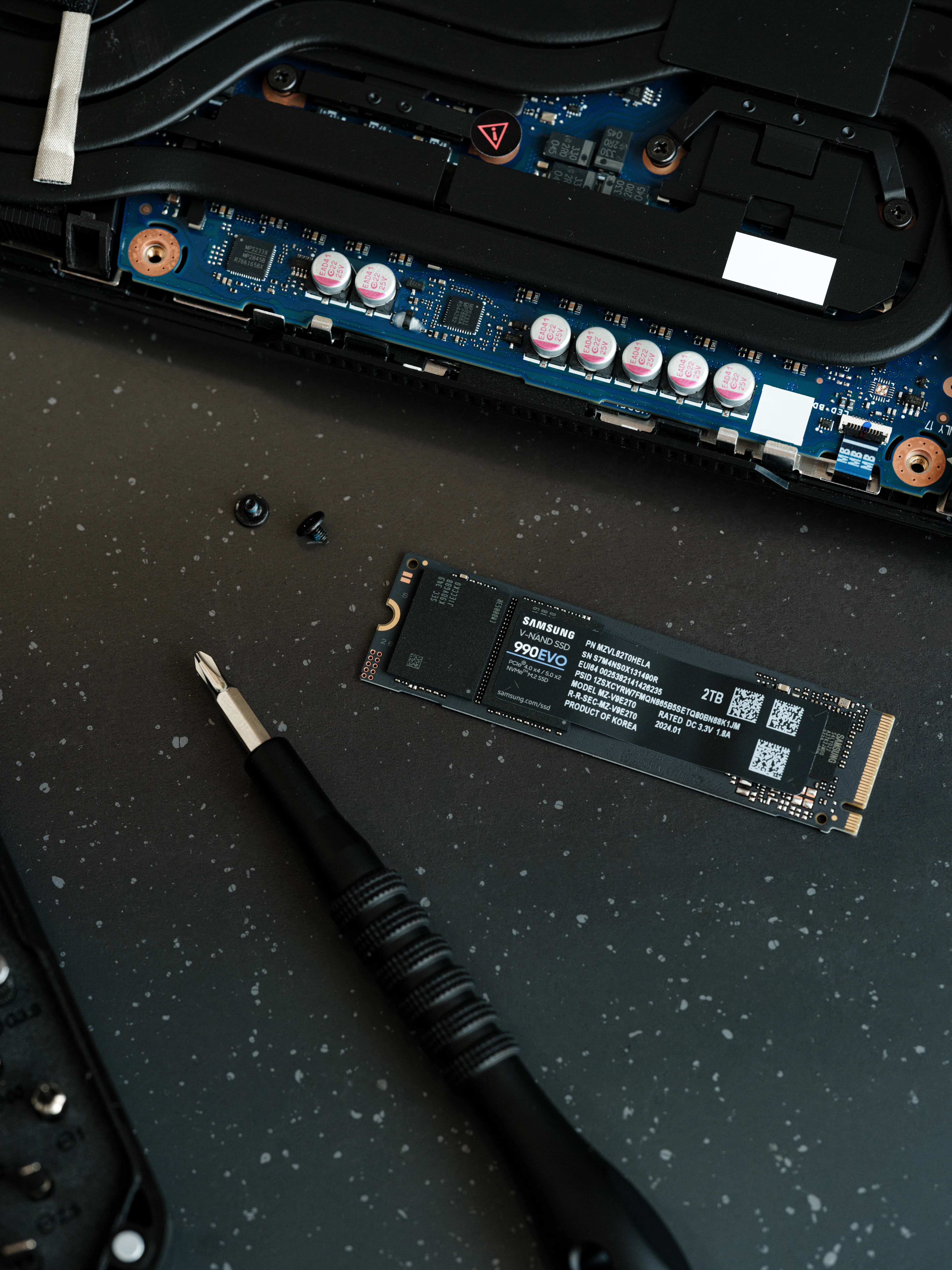 Unità SSD M.2 e cacciavite su un tappetino scuro accanto a una scheda madre