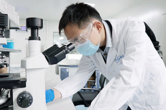 A man in a lab coat and goggles looking through a microscope