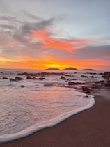 A beach with waves coming in and a sunset in the background