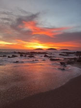 A sunset on a beach with rocks in the water