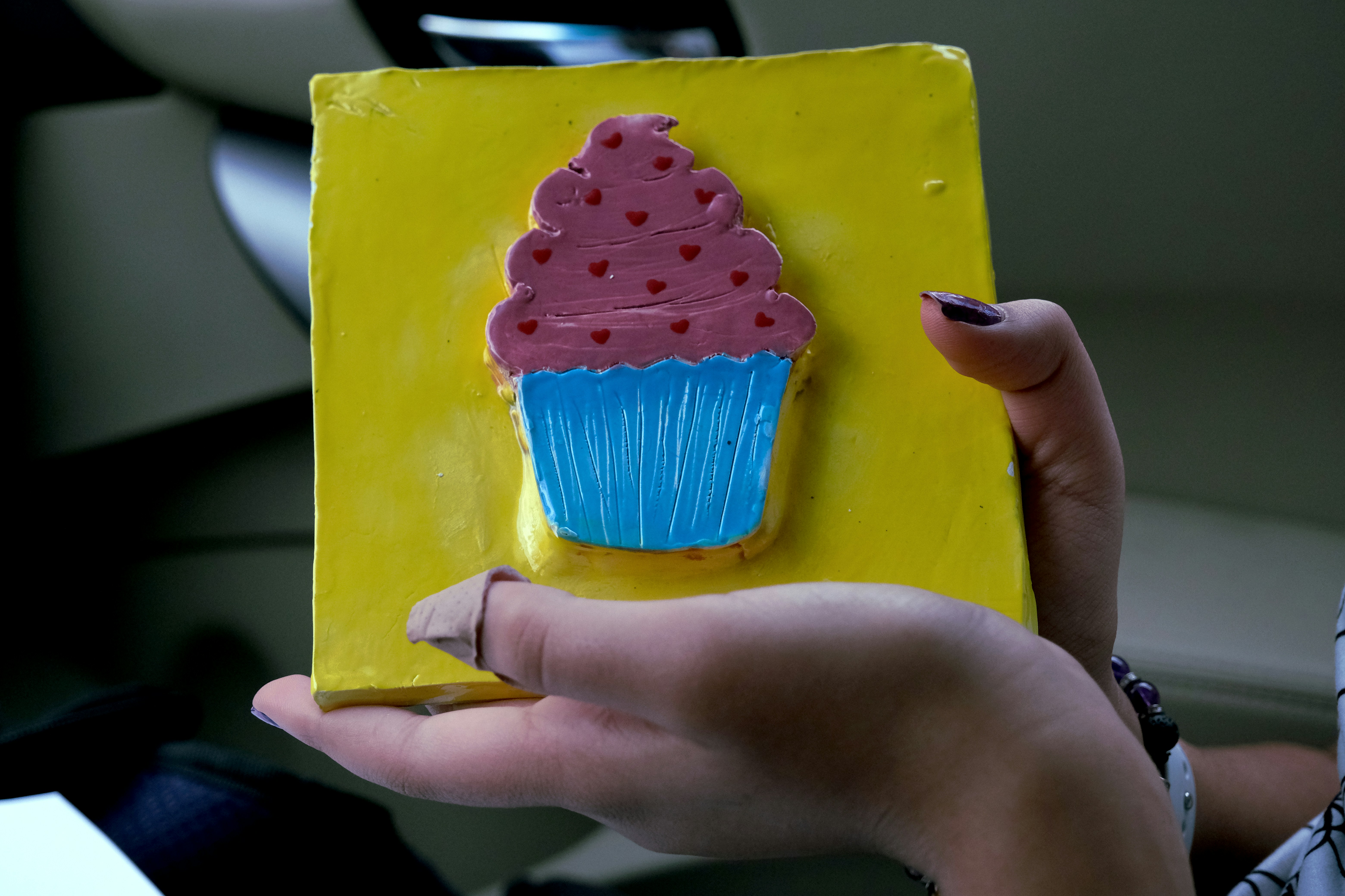 A woman holding a yellow box with a pink frosted cupcake on it