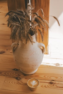 A white vase with a plant in it on a wooden floor