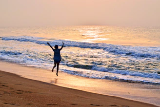A person running on the beach with their arms in the air