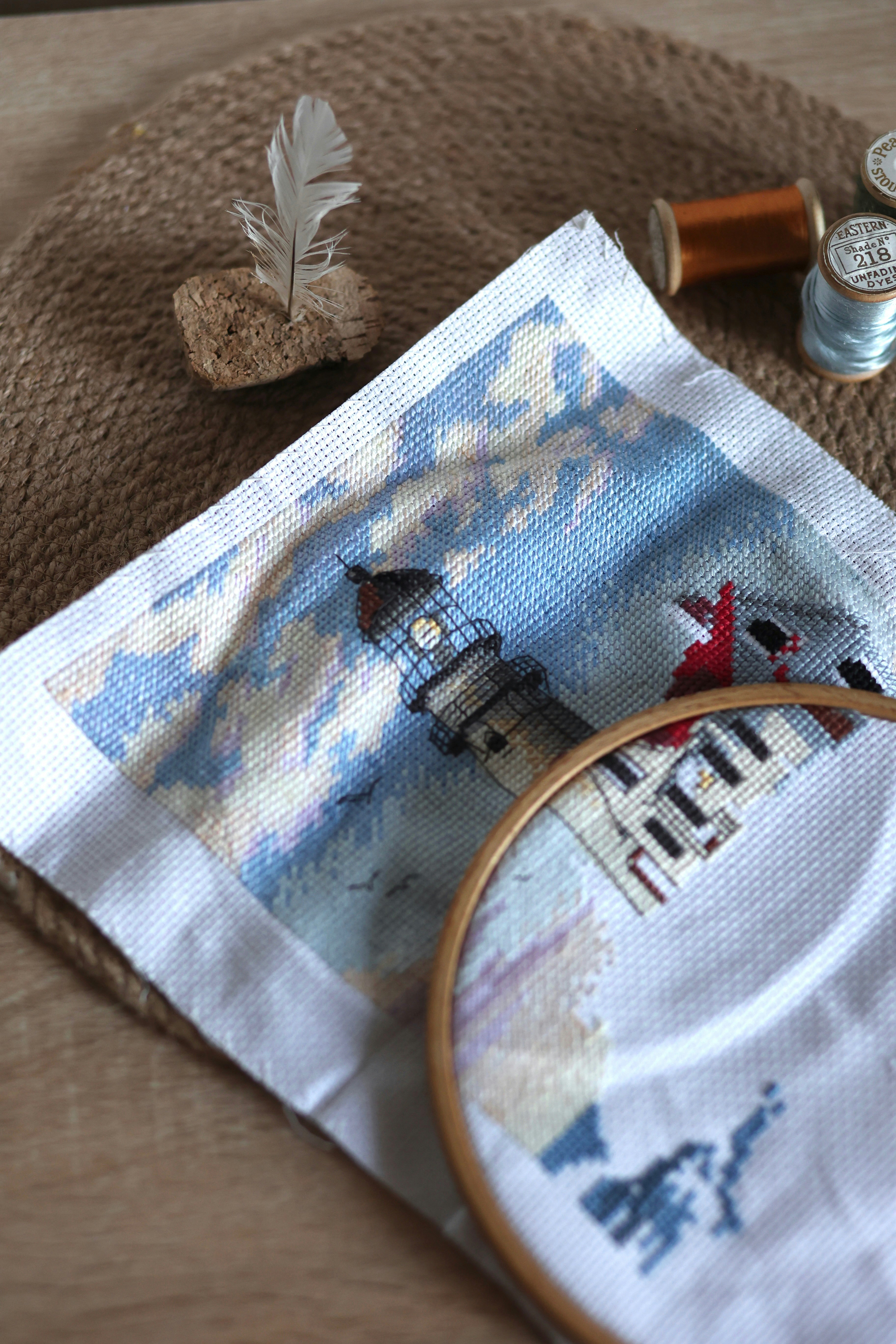 A cross stitch project with a needle and a picture of a lighthouse