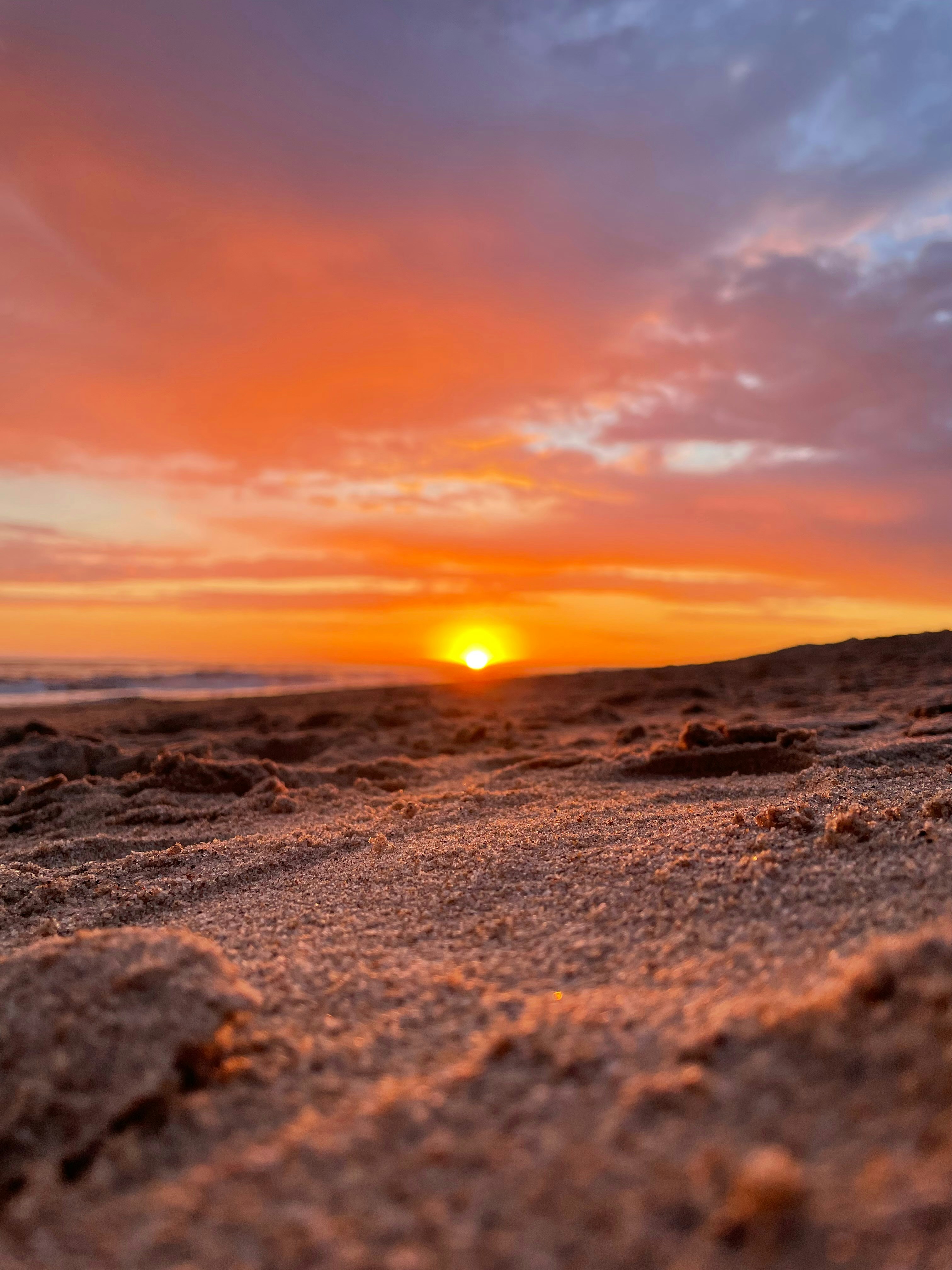 The sun is setting on the beach with sand on the ground