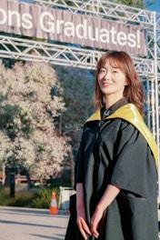 A woman in a graduation gown standing in front of a sign