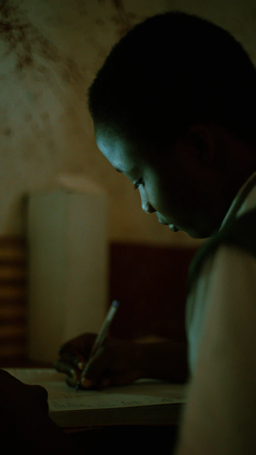 A man writing on a piece of paper in a dimly lit room