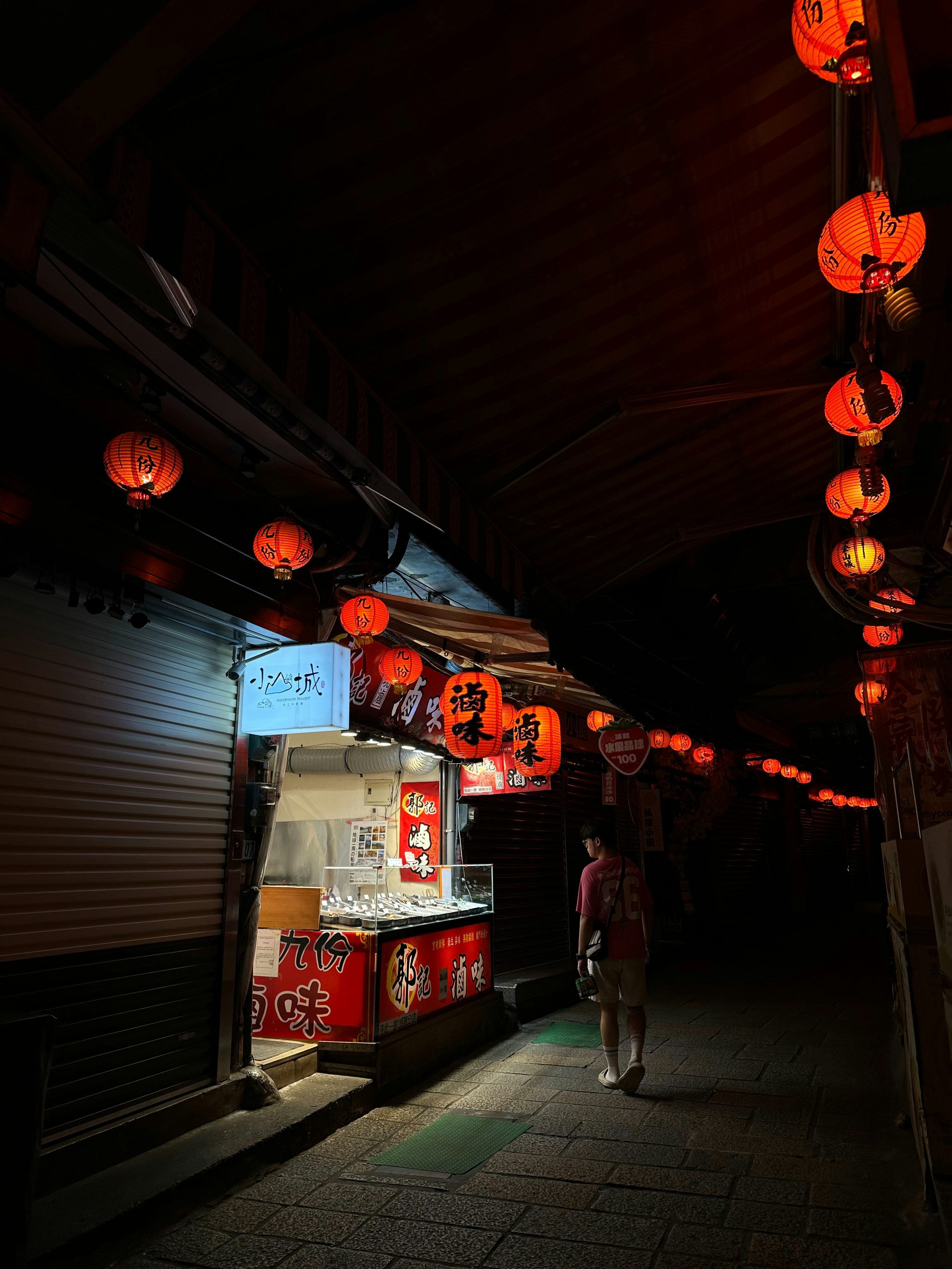 A person walking down a dark alley with lanterns hanging from the ...